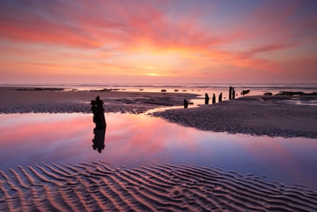 Sunset colours in the sky and reflected in the water pooled on a sandy beach