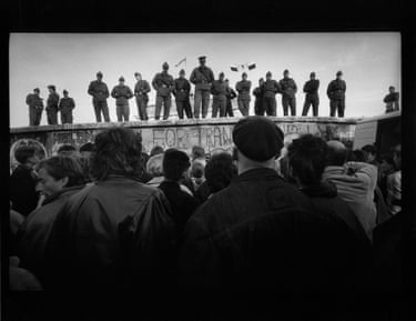 Soldiers stand on top of the wall, looking down at a crowd of people