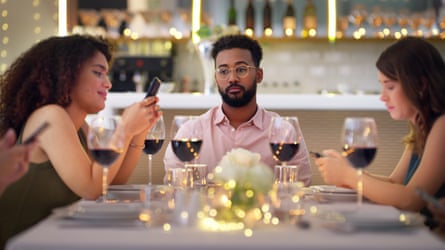 Man sitting look bored as two women with him at restaurant table look at their phones