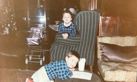 Two children, one leaning over a table drawing and the other sitting on an armchair.