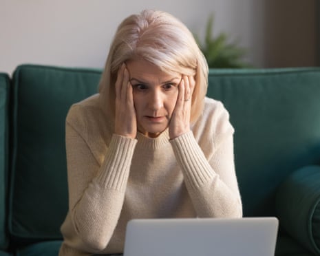 A woman holds her head with both hands, looking worried at a laptop screen