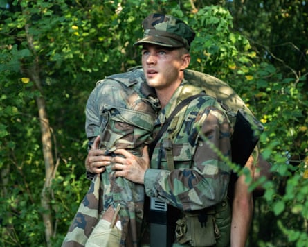 A film still from Netflix’s Boots, in which Miles Heizer holds another actor in a firefighter’s carry, both of them in military camouflage.
