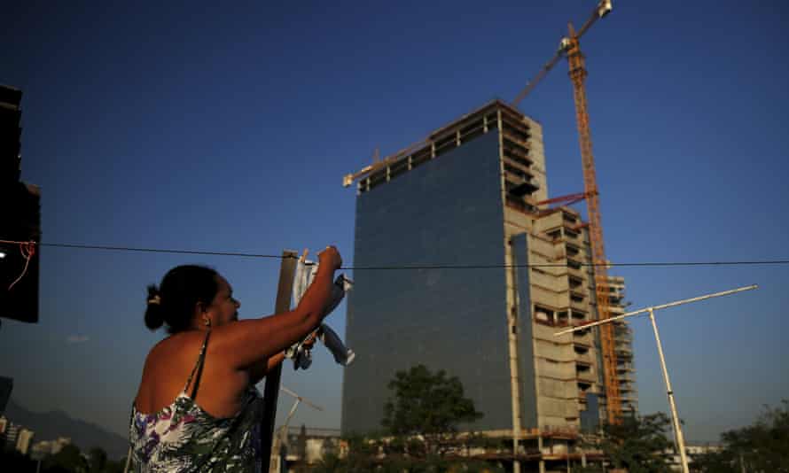 A resident of the Vila Autodromo favela, where about half have left, picks up her clothes in front of the construction work for the Rio 2016 Olympic Park.
