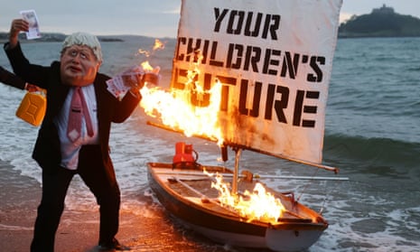 Two activists from Ocean Rebellion, one wearing a Boris Johnson mask and holding money, set a boat on fire during a demonstration ahead of the G7 summit in Cornwall.