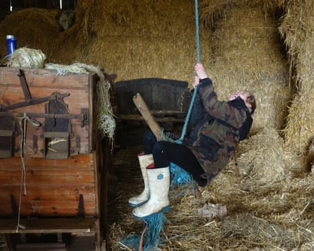 A child swinging from a rope in a barn filled with hay and equipment
