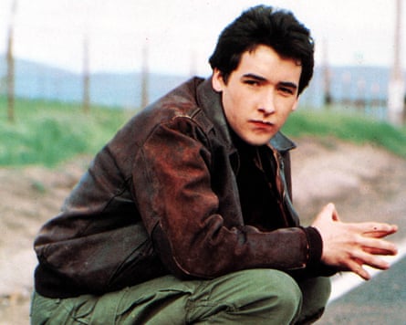 A young John Cusack squats down by the side of the road