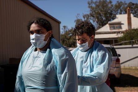Katrina Hunter puts on her PPE gear and is assisted by her uncle Brendon Adams before they drive out to deliver food supplied to people in their community of Wilcannia that have had to isolate due to COVID.