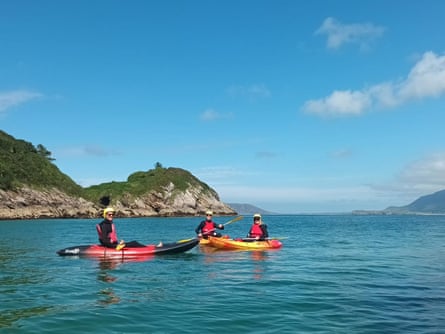 Three kayakers on still blue waters with cliffs behind