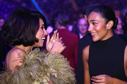 Raye - dressed in a golden dressed trimmer with faux fur - grins and chats with fellow Mercury competitor Olivia Dean, dressed in a black vest