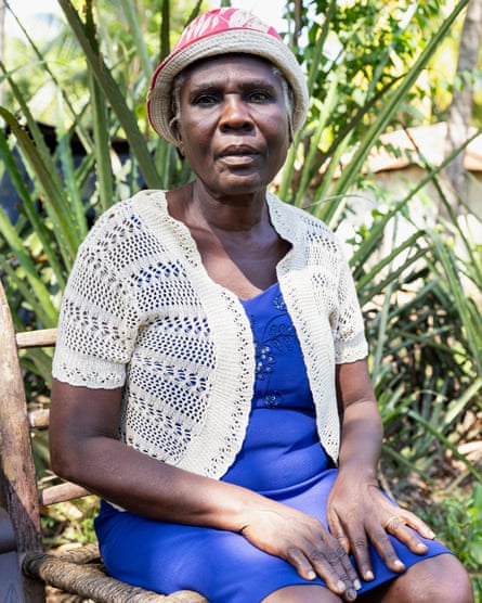 An older woman in a blue dress sits in front of aloe plants