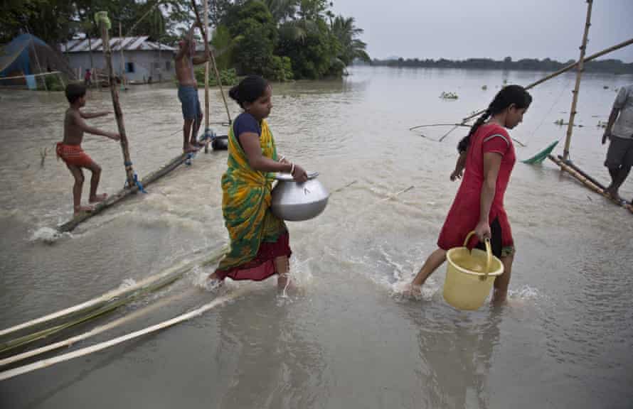 Women carry drinking water across a flooded road in Murkata village, east of Gauhati, Assam state, India.
