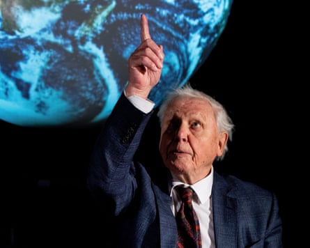 David Attenborough pointing upwards with an image of Earth behind him