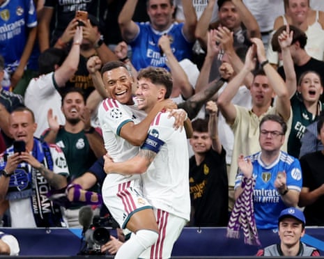 Federico Valverde and Kylian Mbappe embrace joyfully as fans celebrate behind them