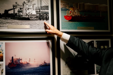 The outstretched arm of a man in a suit points to a picture of a ship on a wall with many pictures of ships.