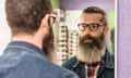 Bearded man in optical store trying on glasses and looking anxious