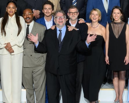 Guillermo del Toro in a dark suit holds his hands up and smiles surrounded by several other people.