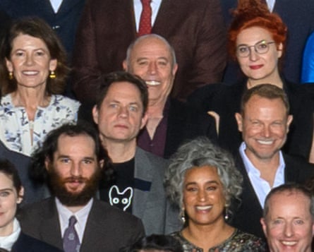 A man in the middle of a group stares into the camera wearing a T-shirt with a picture of a cat.