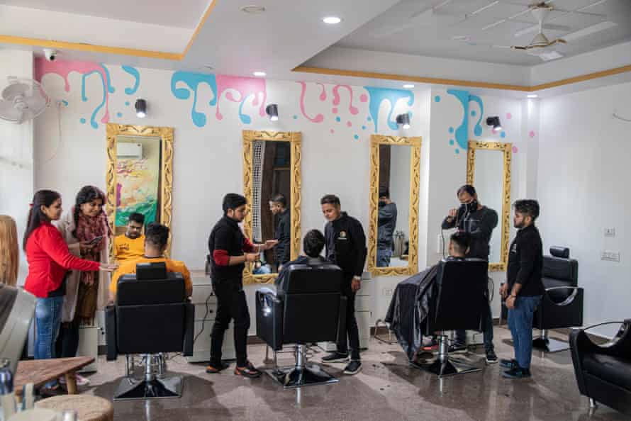 Tree people sit in chairs before mirrors while stylists stand near them