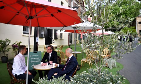 premier Dominic Perrottet and treasurer Matt Kean sit outdoors with owner Jean-Michel Raynaud during a visit to La Renaissance Patisserie and Café in Sydney