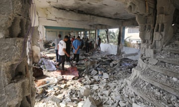Palestinians walk around a damaged, rubble-strewn room