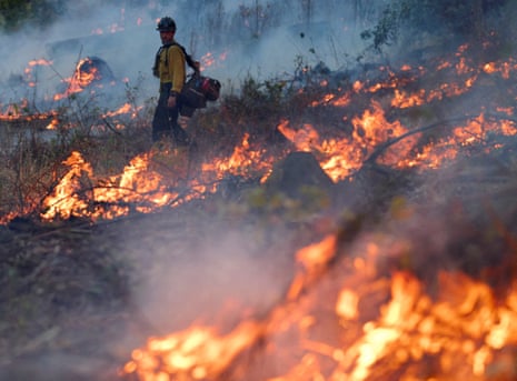 firefighter standing by as fire burns in woodsy area and smoke rises