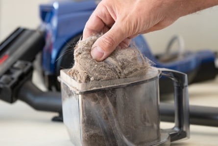 Man’s hand holds dirt and dust out of the vacuum cleaner container and shows it close up with a vacuum cleaner on the background.