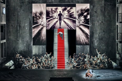 In a scene from the opera Rienzi, a crowd surrounds a red-carpeted staircase as a man collapses, with a couple embracing on the floor