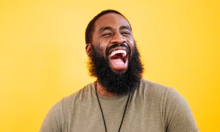 Laughing 31-year-old black manwith short hair and full beard wearing heather T-shirt and laughing while looking away from camera against yellow background.