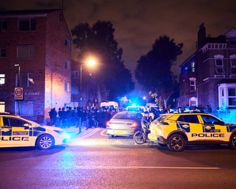 People gather next to police cars on a London street