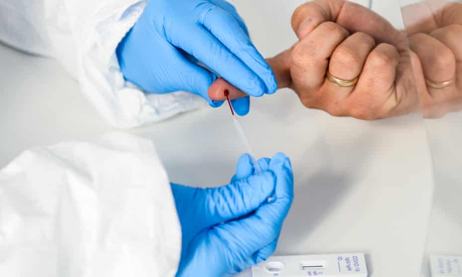 A health worker in a protective suit extracts blood from a patient's finger