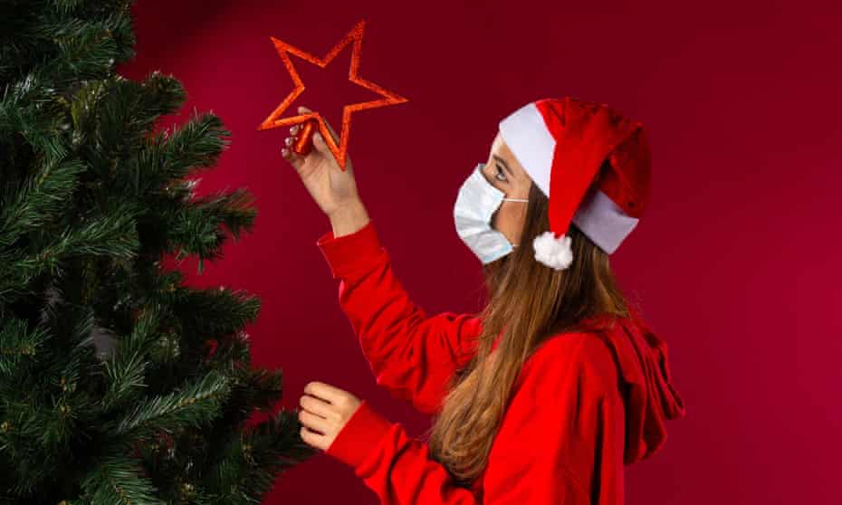A woman in face mask put decorations on a Christmas tree.