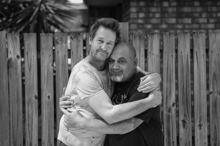Two men hugging in front of a fence in a black and white image