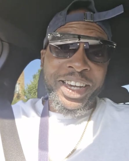 Closeup of Jonathan Stewart talking to a camera. He appears to be in a car. He is black, 40 years old, and wears sunglasses, a back-to-front baseball cap and a white top. He has a beard.