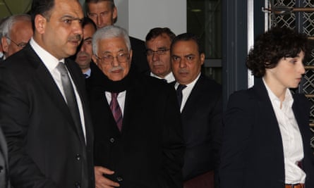 Mahmoud Abbas wearing a suit and a scarf, photographed in a group of people leaving a building