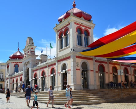 People walk in front of a building with arched windows and wide streamers stretching from the building’s corner tower