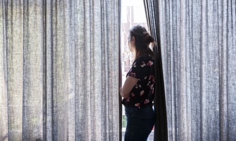 woman looking out window in between curtains