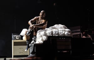 Ja Rule sits on an item of furniture on a stage. Next to him is an old music player on a small cabinet