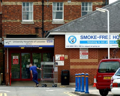 A hospital worker in blue scrubs pushes a metal trolley past the entrance to Leicester General Hospital