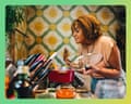 A woman smiles with eyes closed, holding a lid while smelling a pot on a stove
