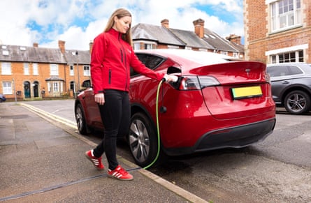 A woman connects an electric car to a charger through a gully in the pavement