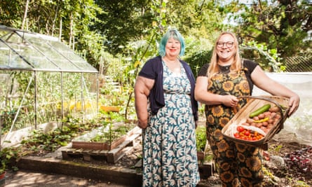 Julia Jepps in a dress and Abbey Fenton, holding a basket of courgettes and tomatoes, next to a greenhouse West Sussex