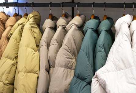 Multicoloured winter down jackets hanging on hangers in the store closeup, side view