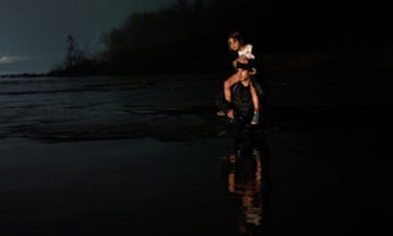 an carrying a young girl wades across the Rio Grande into Eagle Pass from Piedras Negras in Mexico