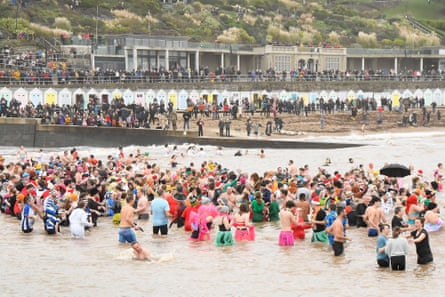 People paddling in the sea watched by lots of people lining the shore