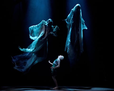 Scorpius, draped in flowing translucent fabric, billows dramatically under dim blue stage lighting