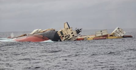 The hull of a ship lying on its side at sea with containers apparently floating beside it
