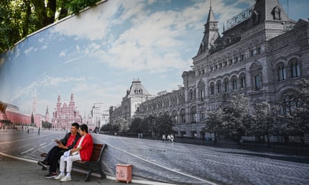 Two people in Beijing sit on a bench in front of a mural depicting Moscow’s Red Square