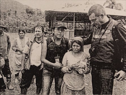 Black and white photo shows a girl crying and a police officer standing beside her in a rural setting. Other people stand in the background