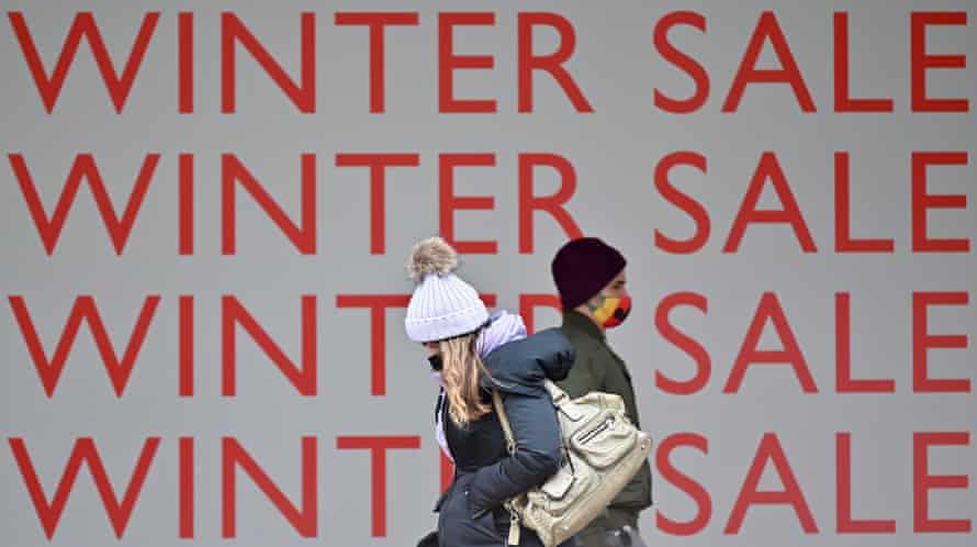 Pedestrians walk past a winter sale sign in the window of a shop
