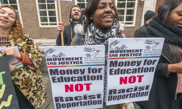 A woman holding two placards reading: 'money for education, not racist deportation'